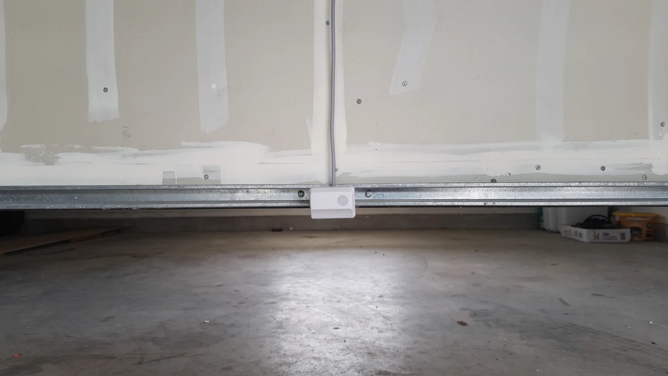 A white safety sensor is attached to the bottom of a garage door.